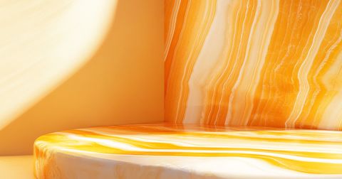 A smooth, polished surface featuring vivid orange and yellow marble streaks, blending beautifully with soft, natural light casting warm shadows.